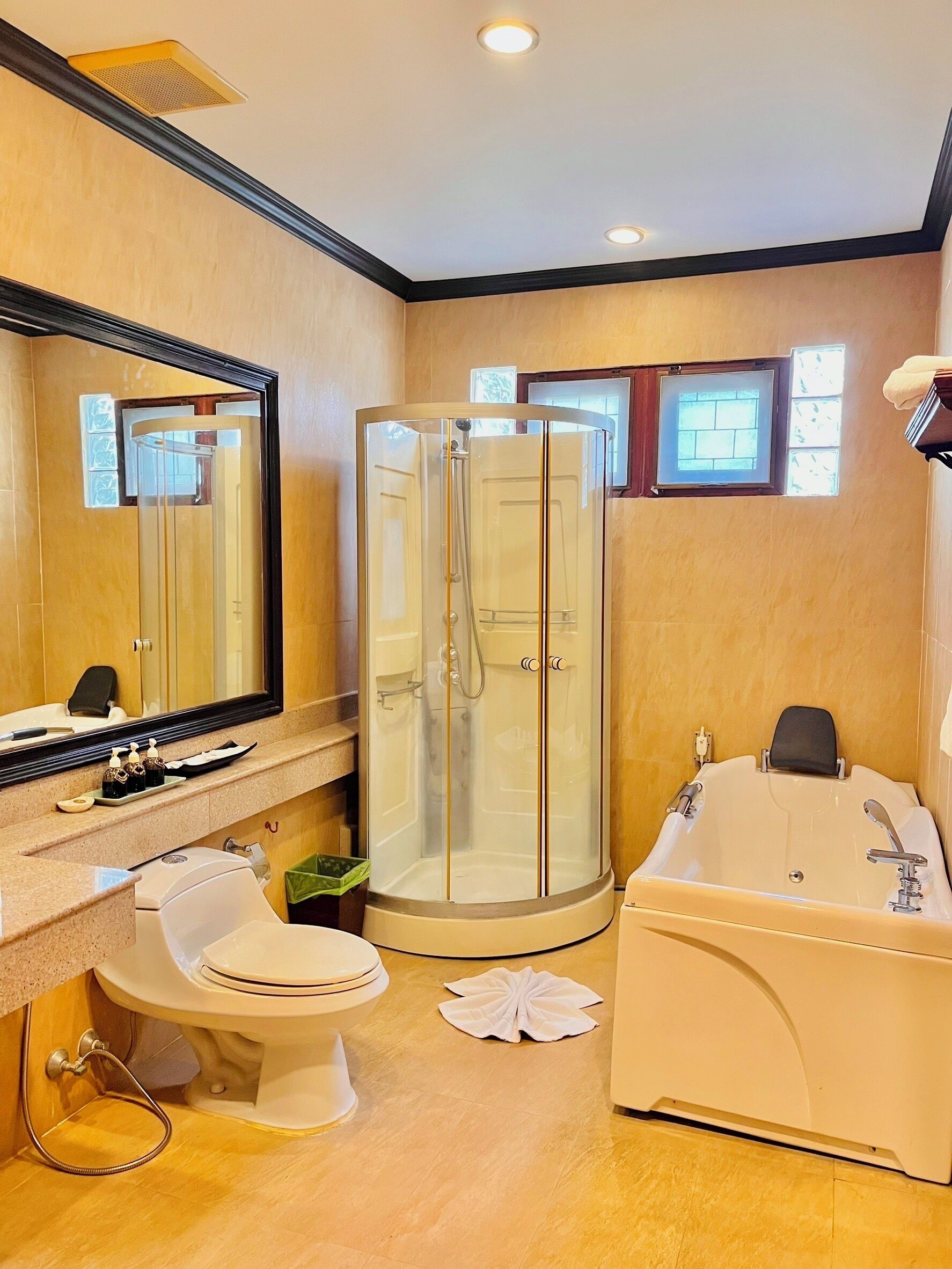 Un baño moderno con ducha envuelta en vidrio, una bañera grande, un inodoro y un tocador con espejo y artículos de aseo.