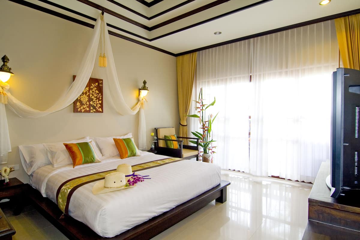 A hotel room with a large bed, a television, a nightstand, and a potted plant.