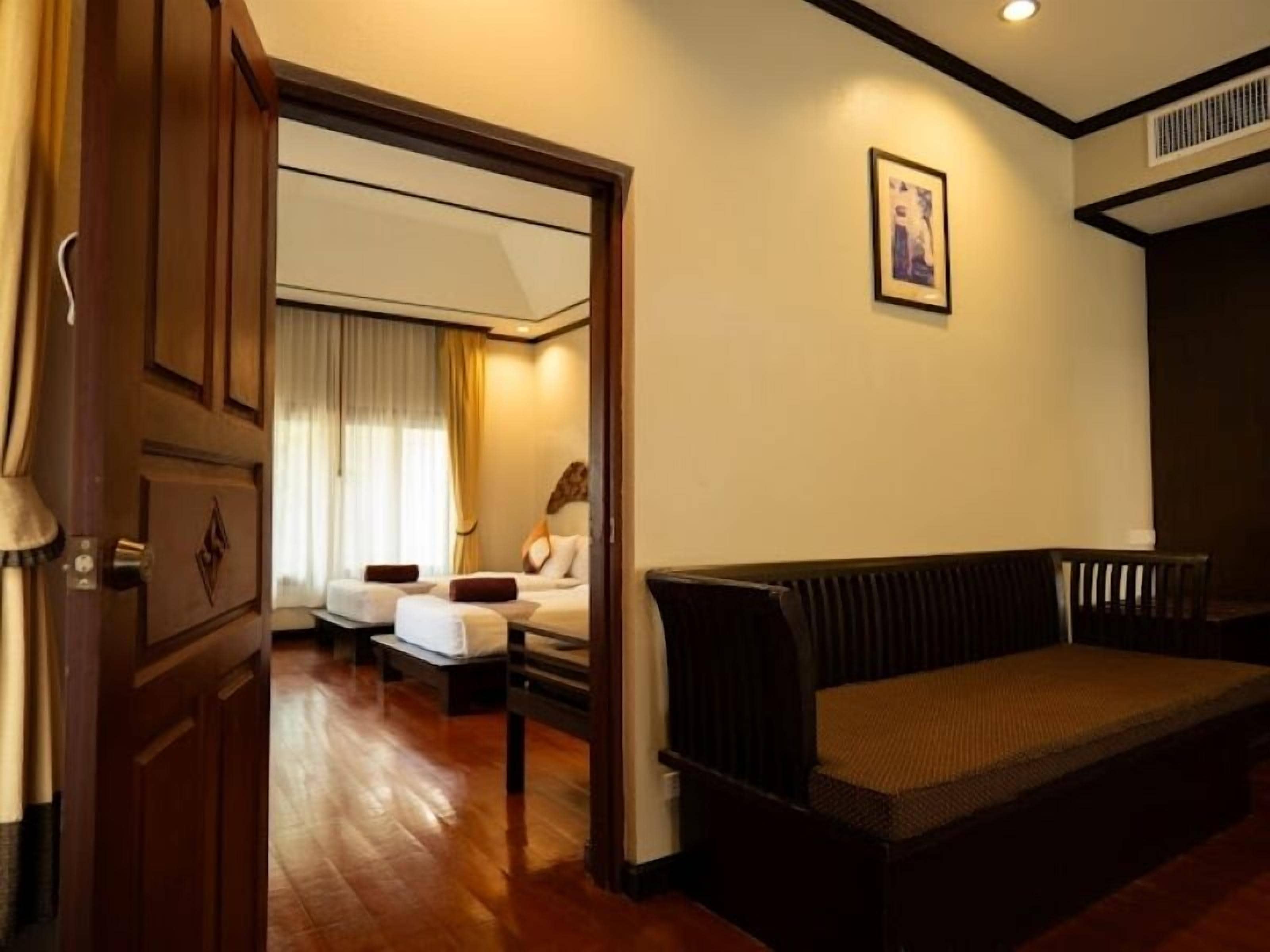 A hotel room with a wooden floor, a sofa, a bed with white linens, a small table, and a window with curtains.