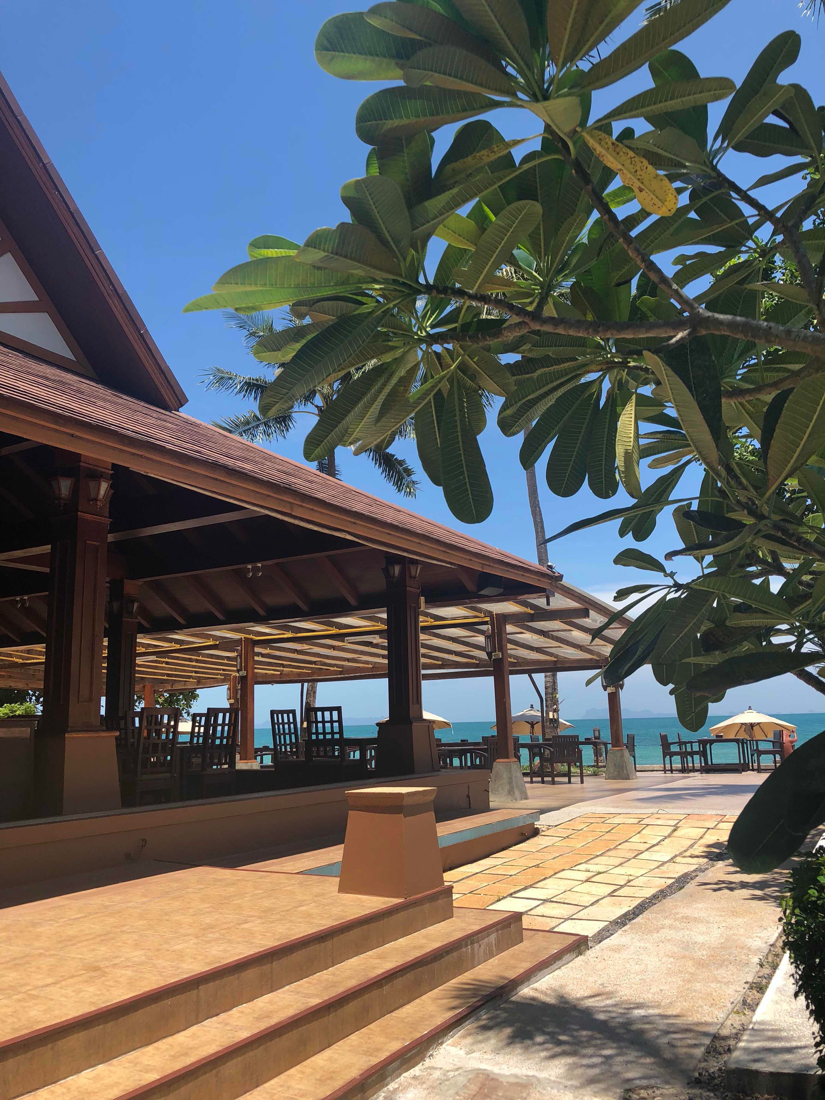 A covered outdoor seating area with wooden furniture and a view of the sea.
