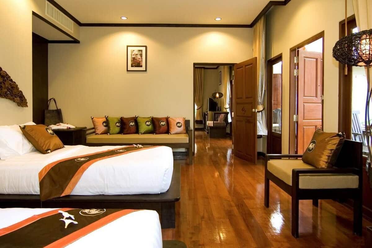Habitación de hotel con dos camas, un sofá, una silla, piso de madera y un pasillo que conduce a un baño.