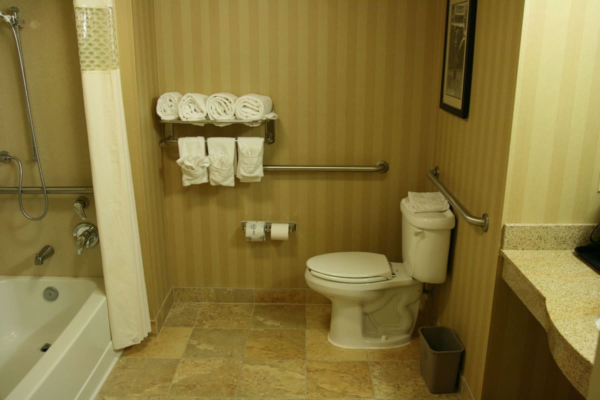 A bathroom with a bathtub, toilet, and a towel rack with towels.