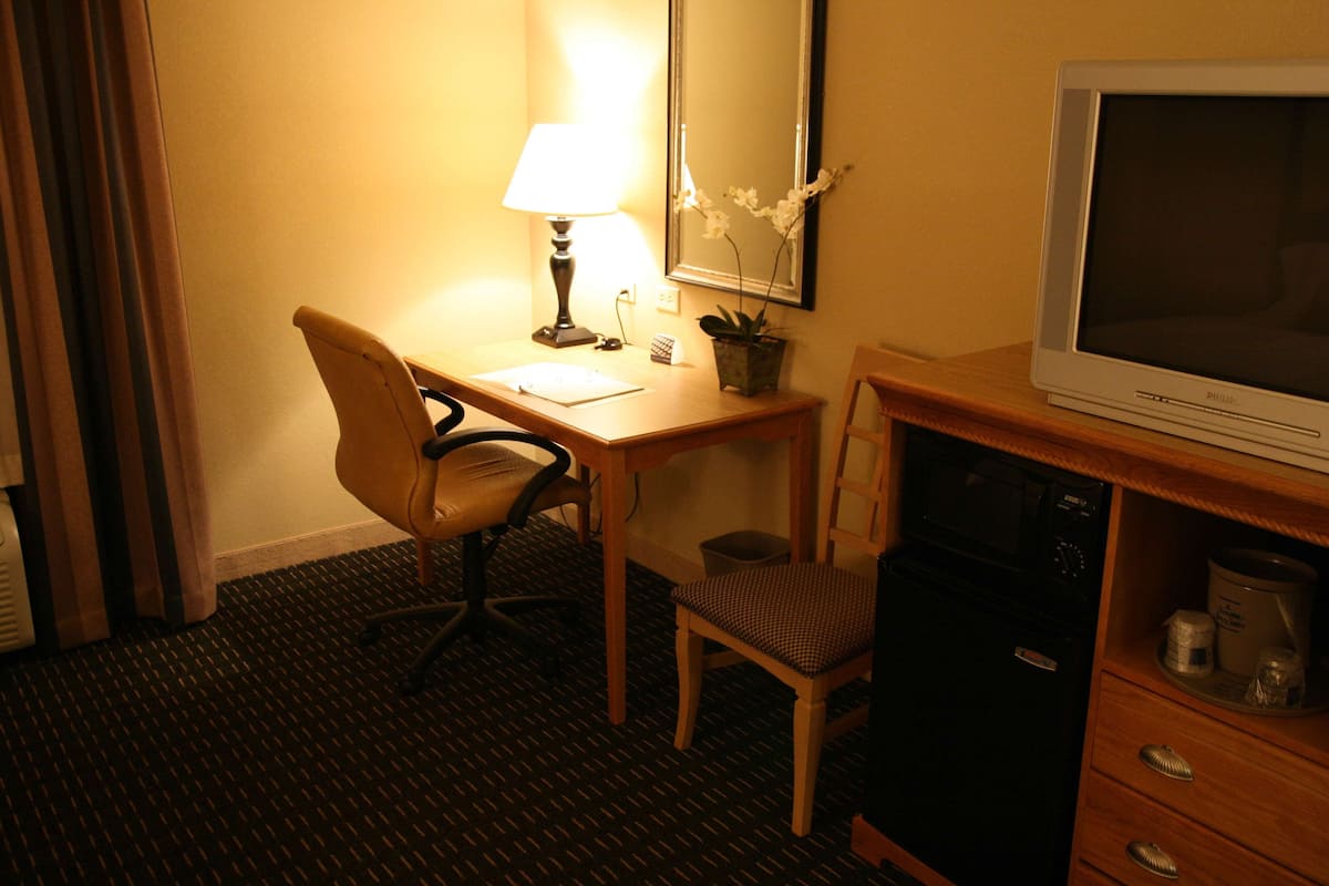 A hotel room with a desk, chair, television, and a small cabinet.