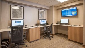 A modern office space with three desks, each with a computer and a chair. There are framed artworks on the walls and a large screen displaying a map. - Hampton Inn & Suites Mobile Providence Park/Airport (Mobile)