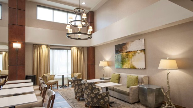 A spacious hotel lobby with a high ceiling, a chandelier, a large abstract painting, and a seating area with tables and chairs. - Hampton Inn & Suites Mobile Providence Park/Airport (Mobile)