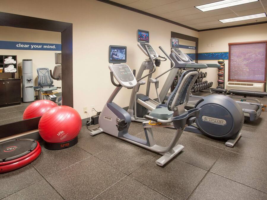 Een fitnessruimte met cardio-apparatuur, rode fitnessballen en een spiegelwand.