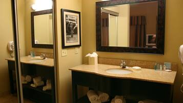 A hotel bathroom with two sinks, a large mirror, and towels neatly stacked on shelves.