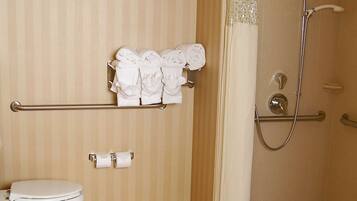 A bathroom with a toilet, a towel rack with towels, a shower with a handheld showerhead, and a toilet paper holder.