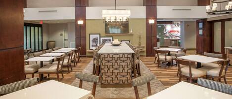 A spacious restaurant with high ceilings, multiple dining tables, and a central decorative island.