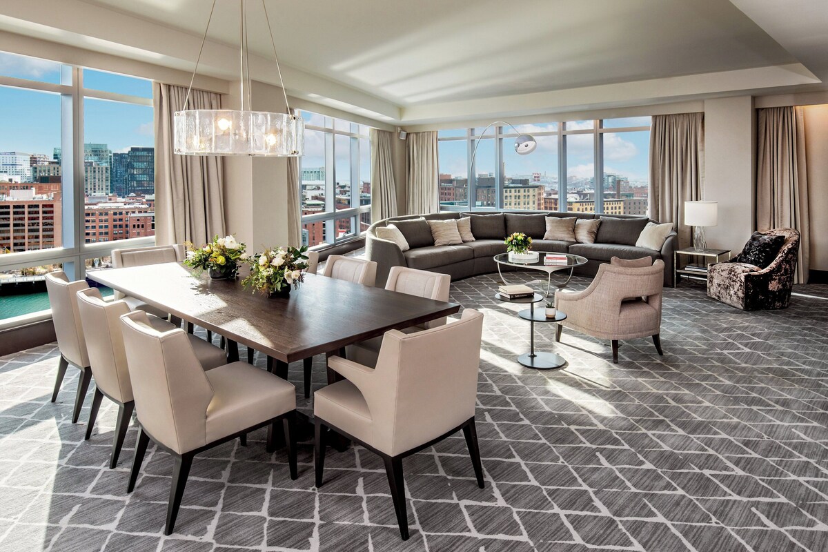 Una sala de estar moderna con comedor, ventanas amplias y vista a la ciudad.