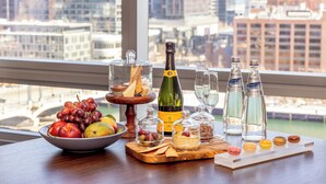 A table with a variety of food and drink items, including a bottle of champagne, glasses, and macarons, set against a cityscape view. - InterContinental Boston by IHG (Boston)