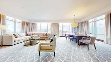 Ein geräumiges Hotelzimmer mit einer großen Couch, einem Esstisch und einem Couchtisch. Das Zimmer verfügt über große Fenster mit Vorhängen und Blick auf die Stadt.