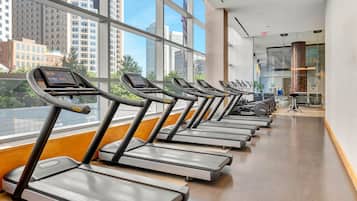 A row of treadmills in a gym with large windows and a view of city buildings.