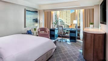 Quarto de hotel com uma cama grande, uma escrivaninha com computador, uma cadeira, uma mesinha e uma televisão.