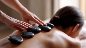 A person receiving a stone massage with several black stones placed on their back.