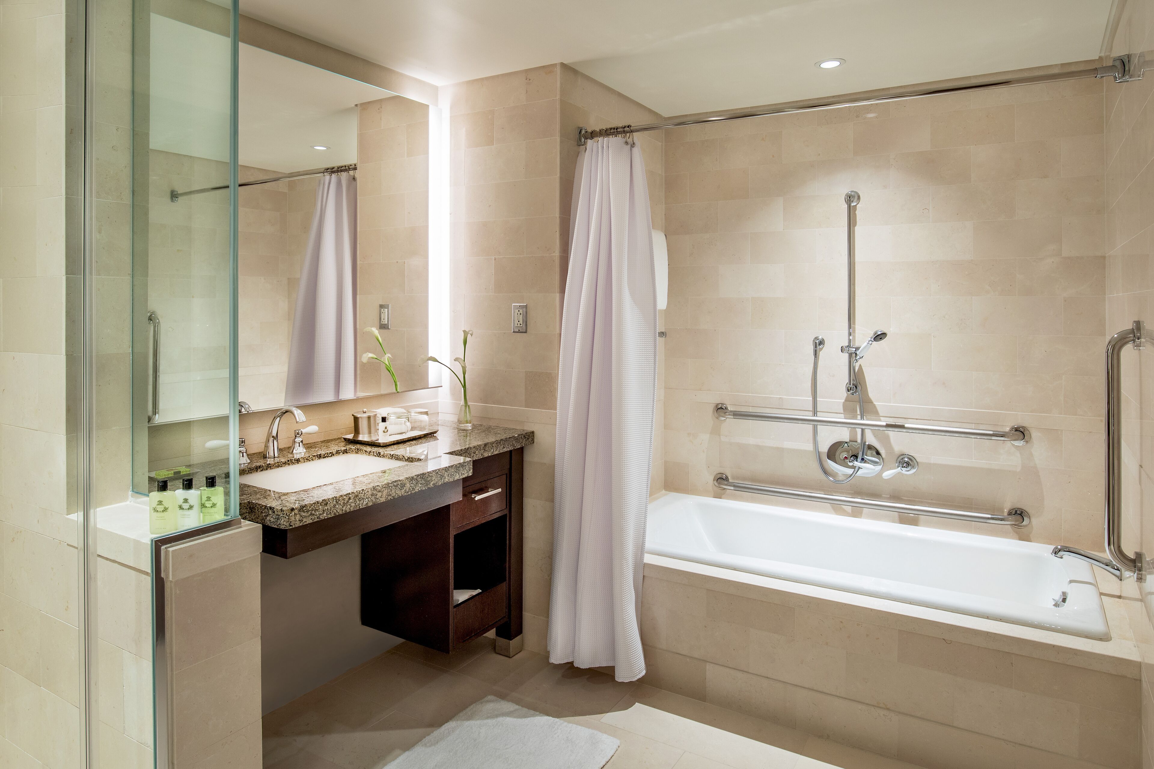 A modern bathroom with a glass shower enclosure, a sink with a vanity, and a bathtub with grab bars.