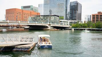 Un río con un puente, una barca amarrada en un muelle y edificios modernos al fondo.