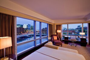 A hotel room with a large window offering a city view, a bed, a chair, a desk, and a lamp. - InterContinental Boston by IHG (Boston)