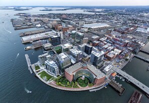 An aerial view of a waterfront cityscape with a prominent circular building surrounded by smaller structures, a bridge, and a marina with boats. - InterContinental Boston by IHG (Boston)