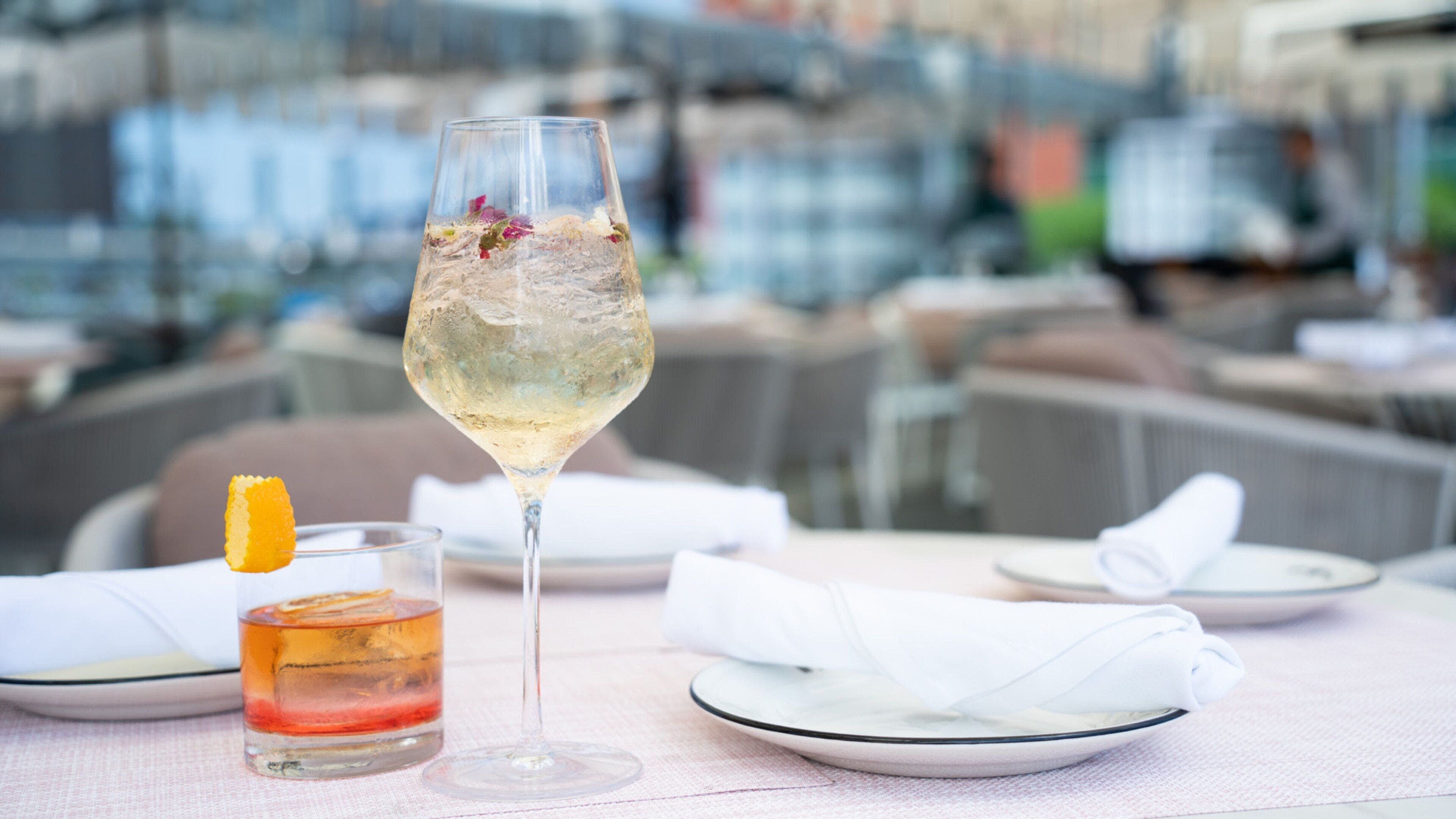 A table with a glass of white wine, a glass of red wine, and a cocktail with an orange garnish.