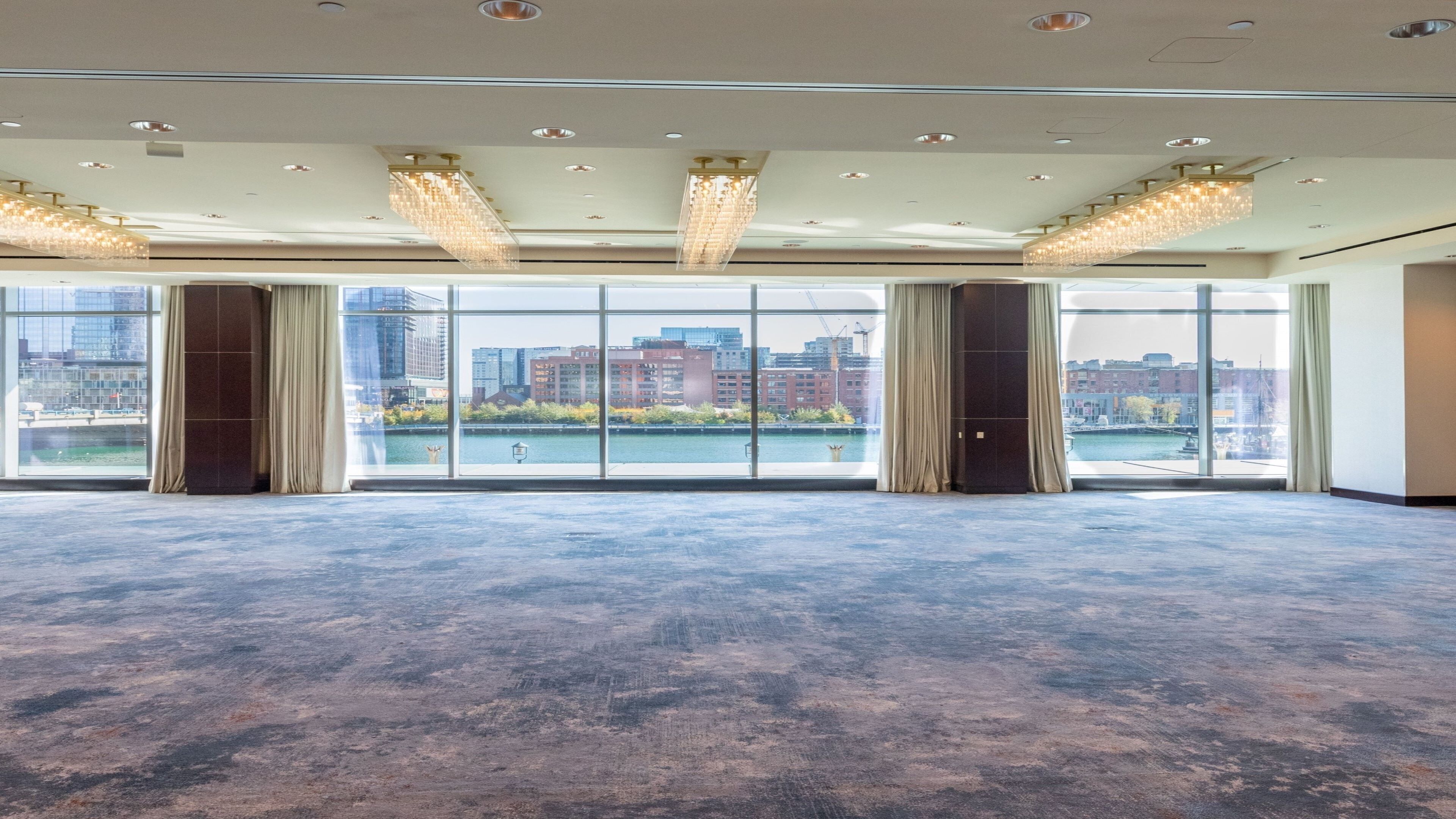 A spacious room with large windows offering a view of a cityscape and a river.