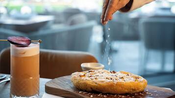 A hand sprinkling salt over a dessert on a wooden board, next to a glass of a layered beverage.