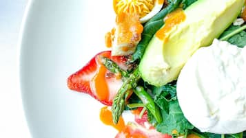 A white plate with a salad consisting of avocado, tomato, asparagus, and a poached egg.