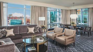 A hotel room with a large window, a sofa set, a coffee table, and a dining area.