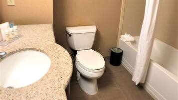 Une salle de bain avec un lavabo sur un plan de travail en granit, des toilettes et une douche avec un rideau blanc.