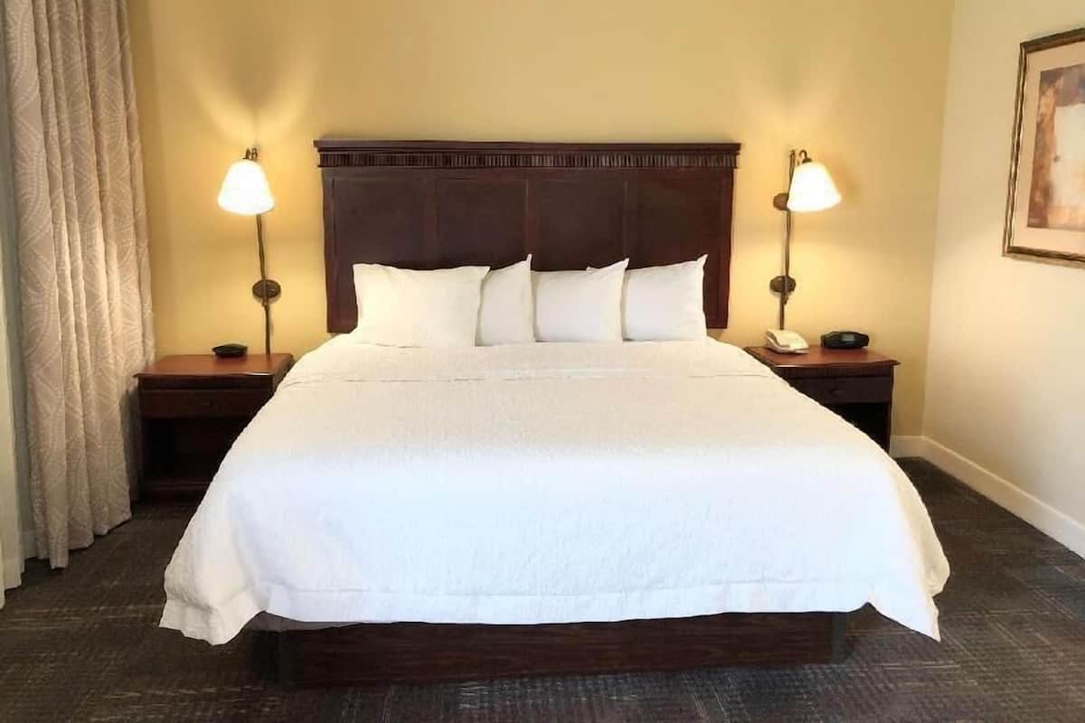 A hotel room with a large bed, two bedside tables, a headboard, and two wall-mounted lamps.
