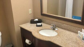A bathroom with a sink, mirror, toilet, and a trash can.