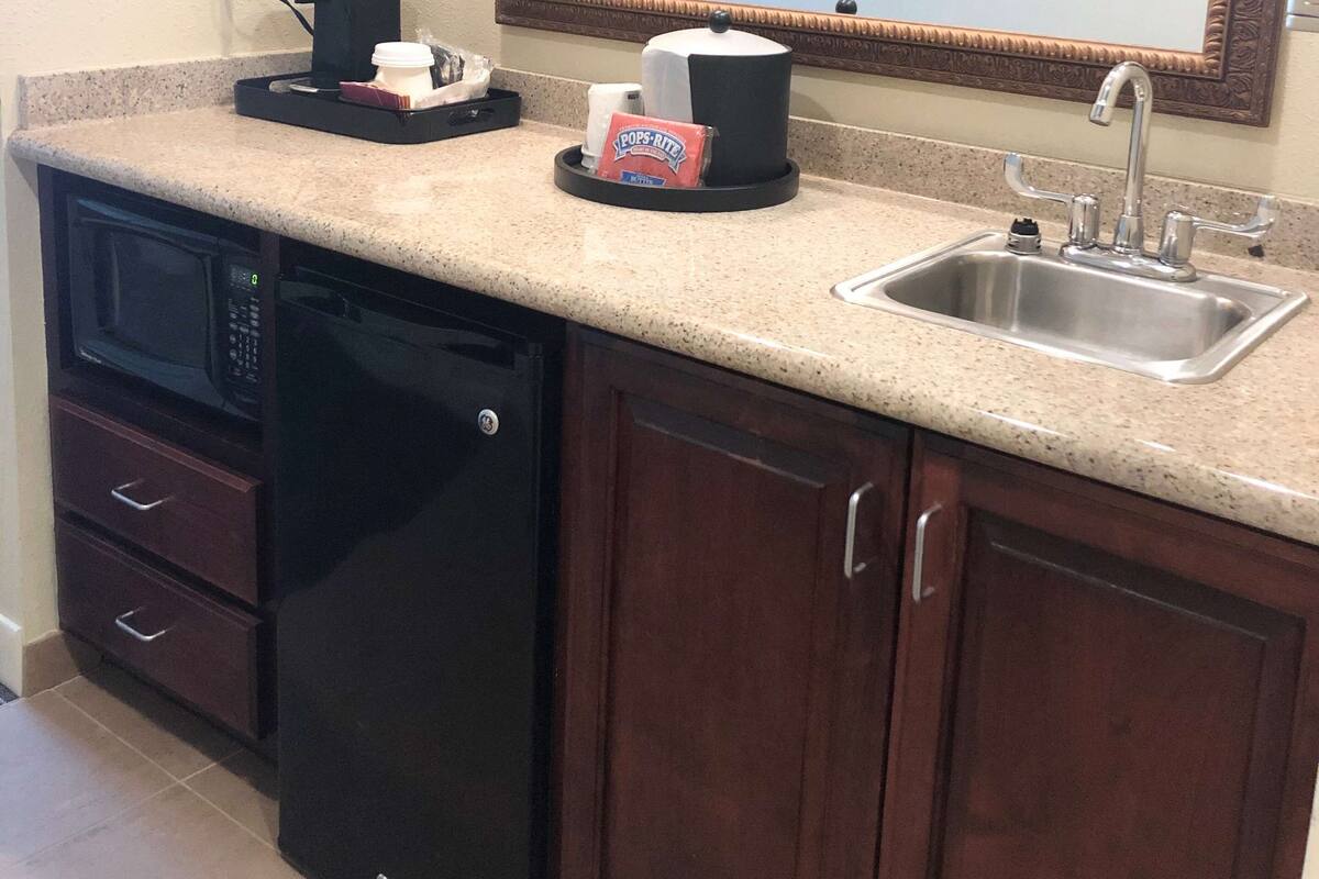 A compact kitchen with a built-in dishwasher, a coffee maker, a sink, and a mirror above the countertop.