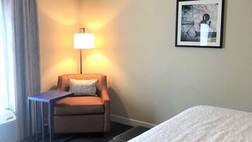 Une chambre d’hôtel avec un lit, une chaise, une table, une lampe et un tableau encadré au mur.