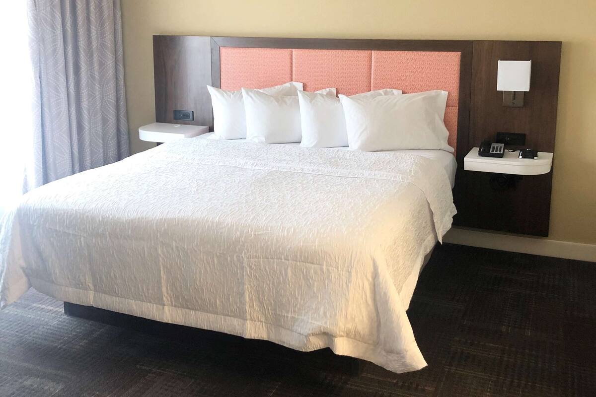 A hotel room with a large bed, a nightstand, a bedside table, and a window with curtains.