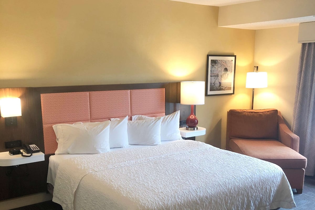 A hotel room with a large bed, two bedside tables with lamps, a chair, and a framed picture on the wall.