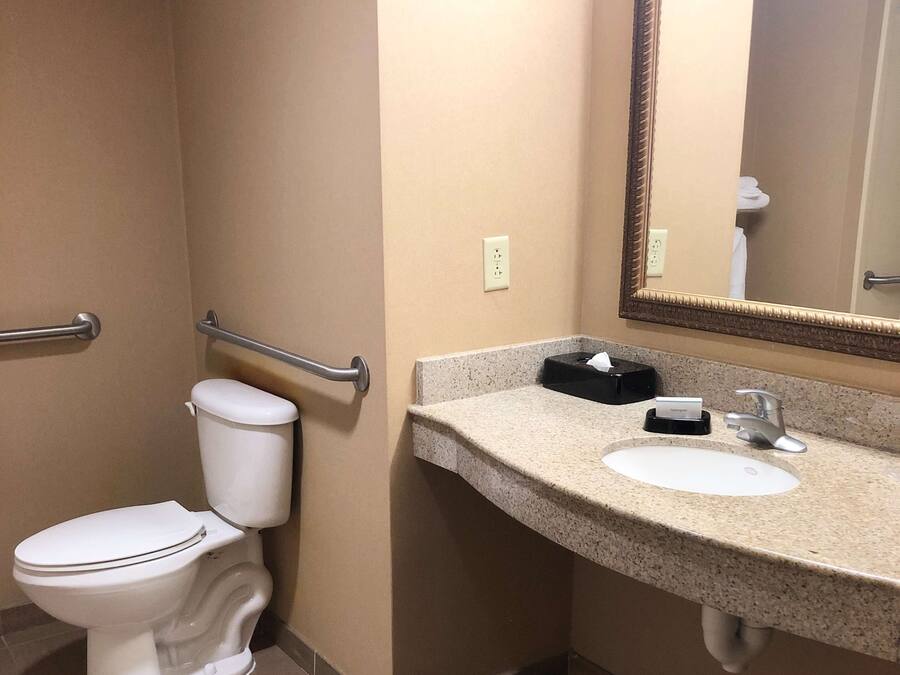 Un baño con inodoro, lavamanos, espejo y barandilla.