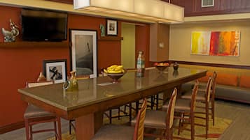 A modern dining area with a long wooden table, cushioned chairs, a television, and decorative items.