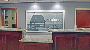 A reception desk with a framed picture of a beach scene and the word "explore." - Hampton Inn & Suites Norfolk-Airport (Norfolk)