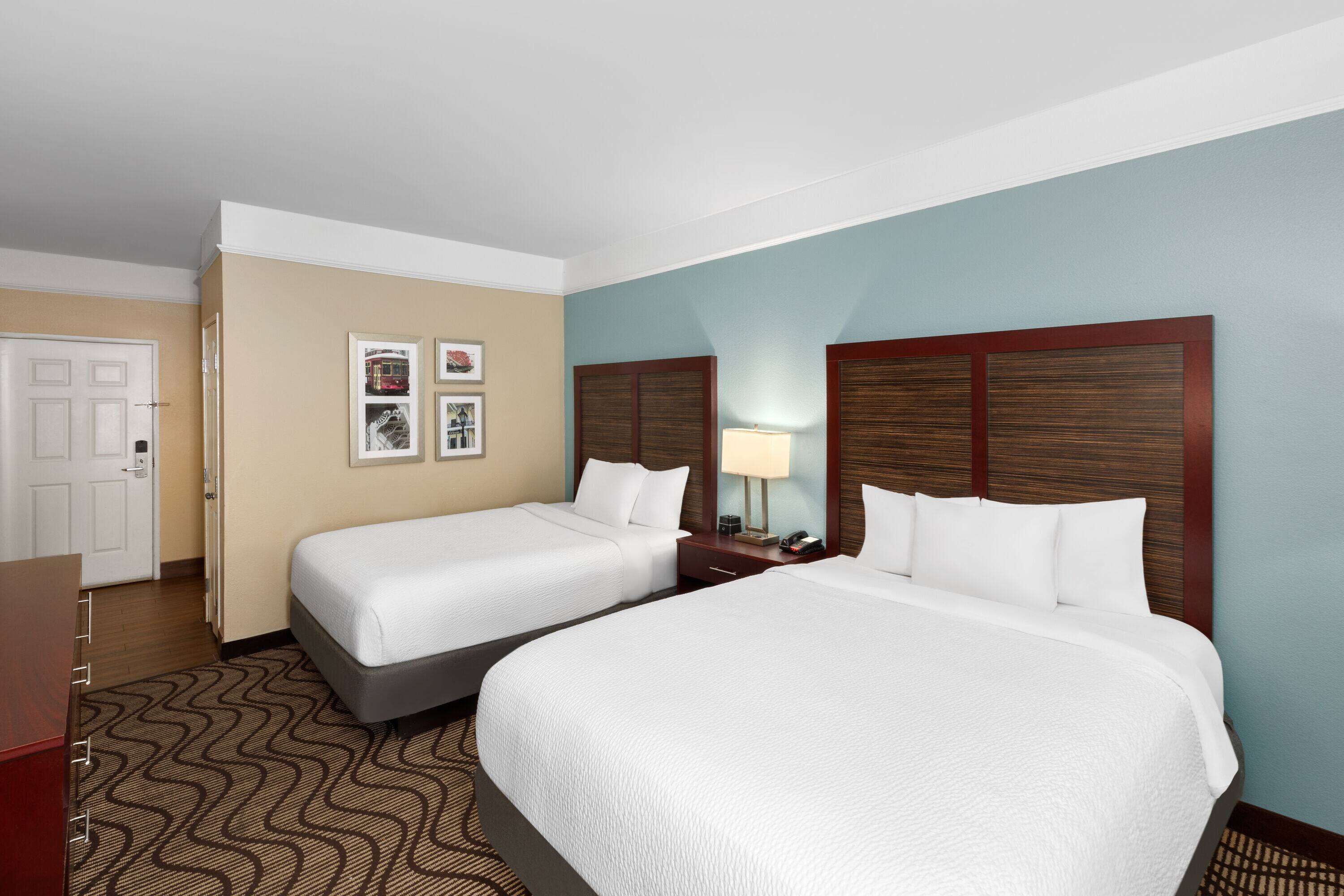 A hotel room with two beds, a desk, a chair, and a door.