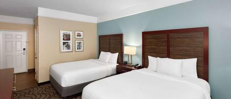 A hotel room with two beds, a desk, a chair, and a door.