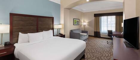A hotel room with a large bed, a desk, a chair, a television, and a window with curtains.