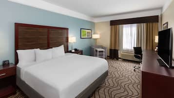Une chambre d’hôtel avec un grand lit, un bureau doté d’un téléviseur à écran plat, une chaise, une lampe de bureau, une petite table et une fenêtre avec des rideaux.