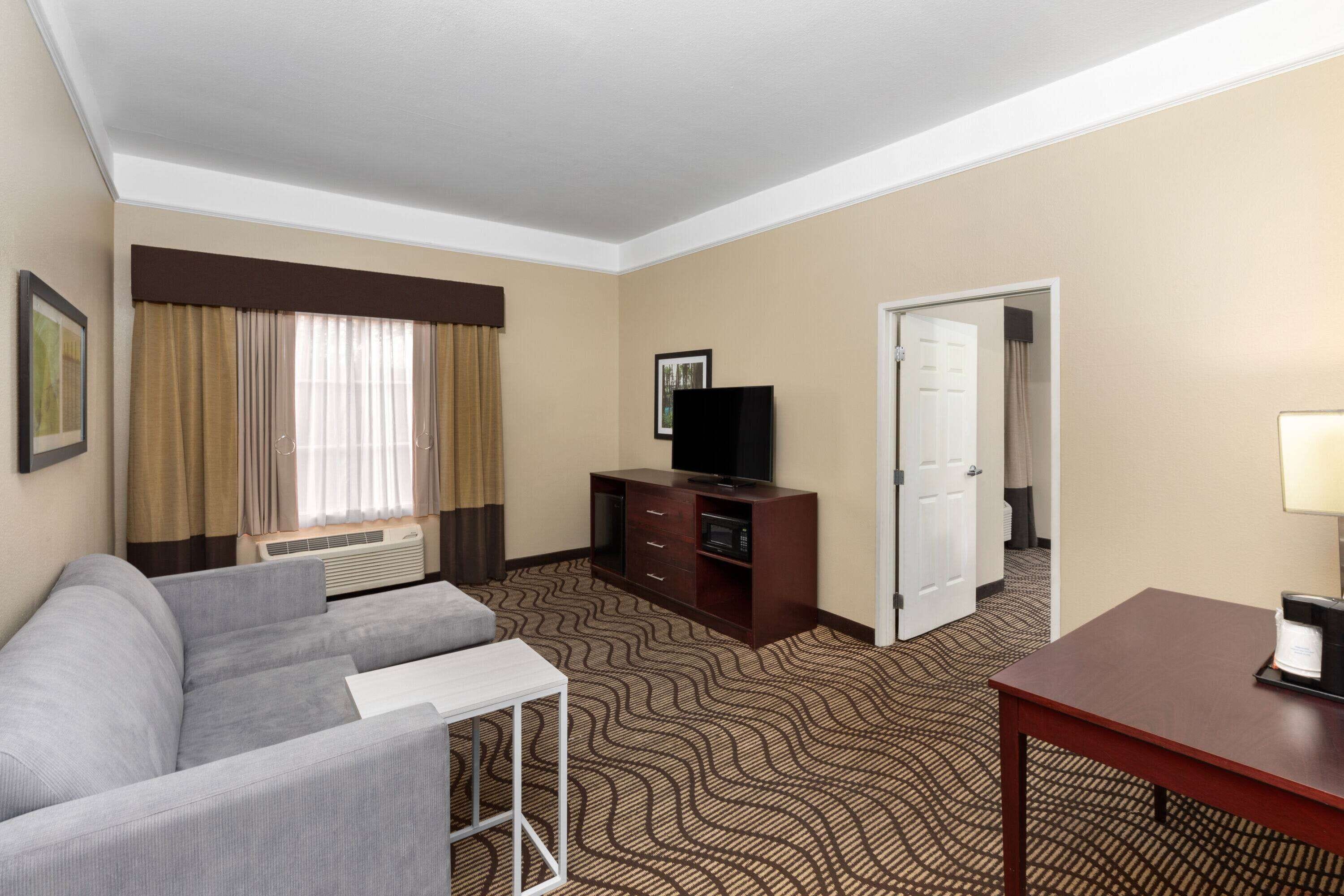 A hotel room with a sofa, a TV, a small table, and a patterned carpet.