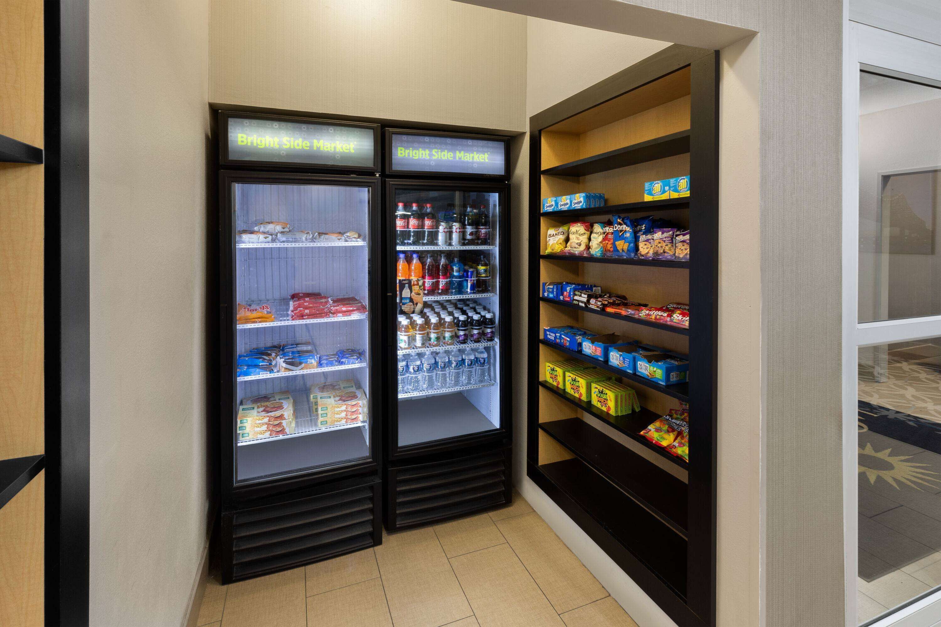 A section of a store with two refrigerated display cases labeled "Bright Side Market" and shelves stocked with snacks and beverages.