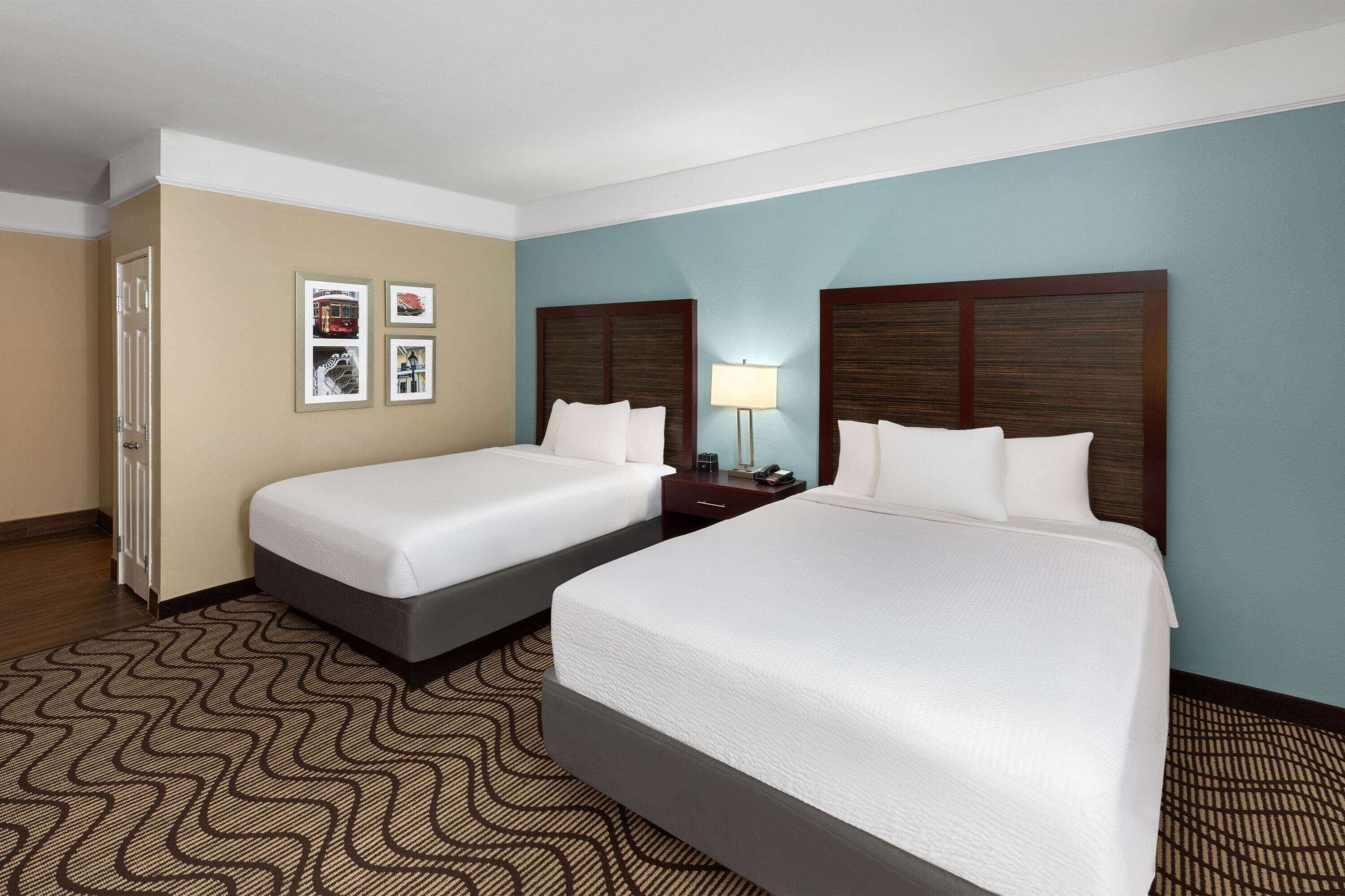 A hotel room with two beds, a nightstand, a lamp, and framed pictures on the wall.