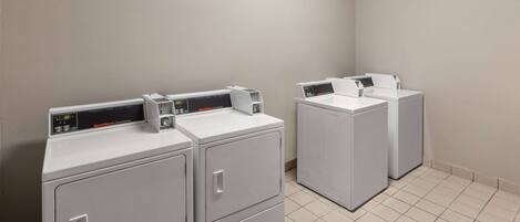 A laundry area with three stacked washers and dryers, a control panel, and a tiled floor.