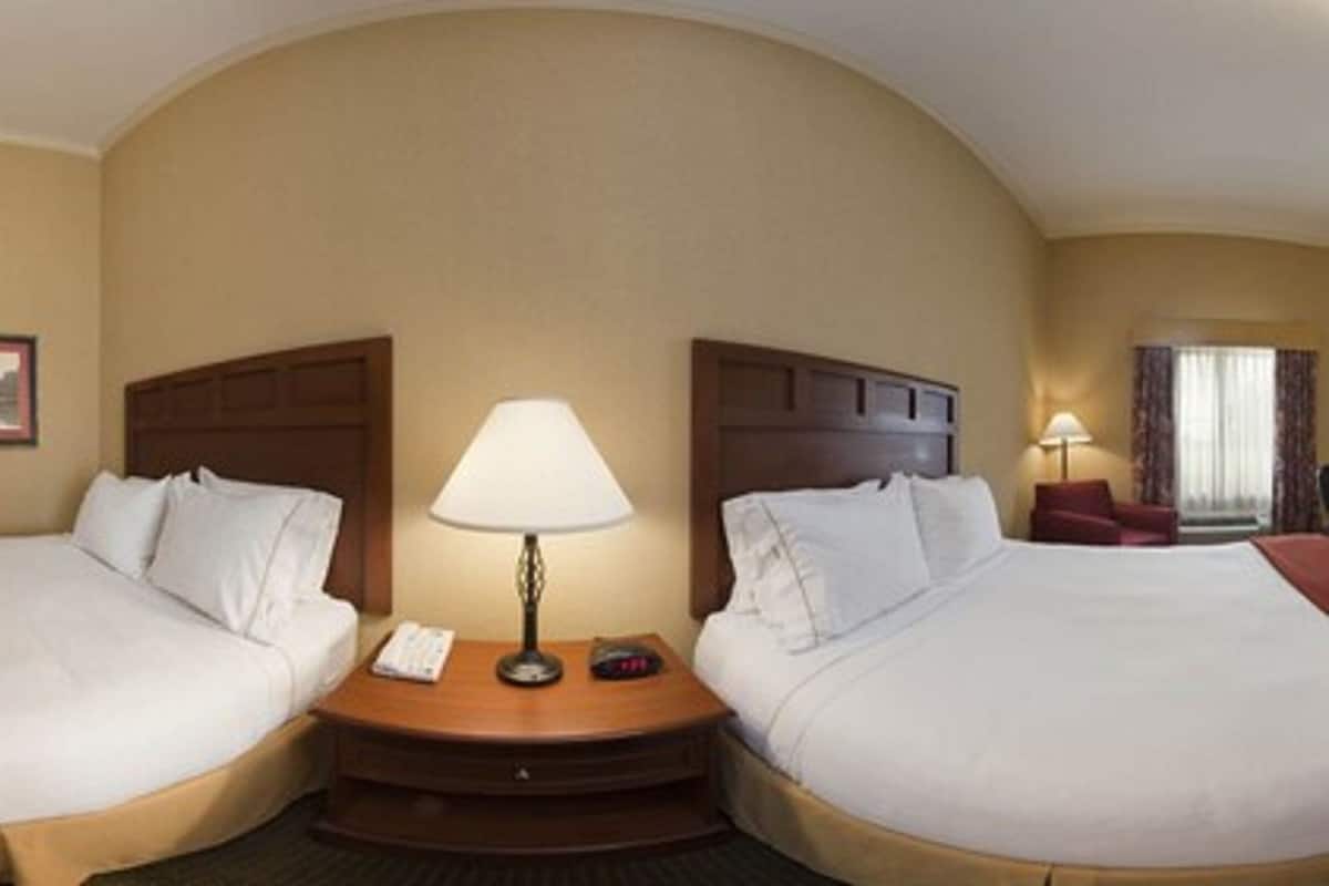 A hotel room with two beds, a nightstand with a lamp, a framed picture on the wall, and a window with curtains.