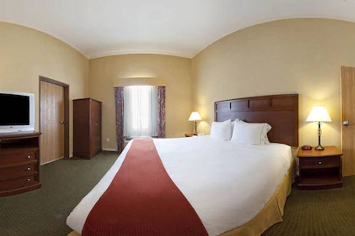 A hotel room with a large bed, two bedside tables with lamps, a television, a wardrobe, and a door leading to another room.
