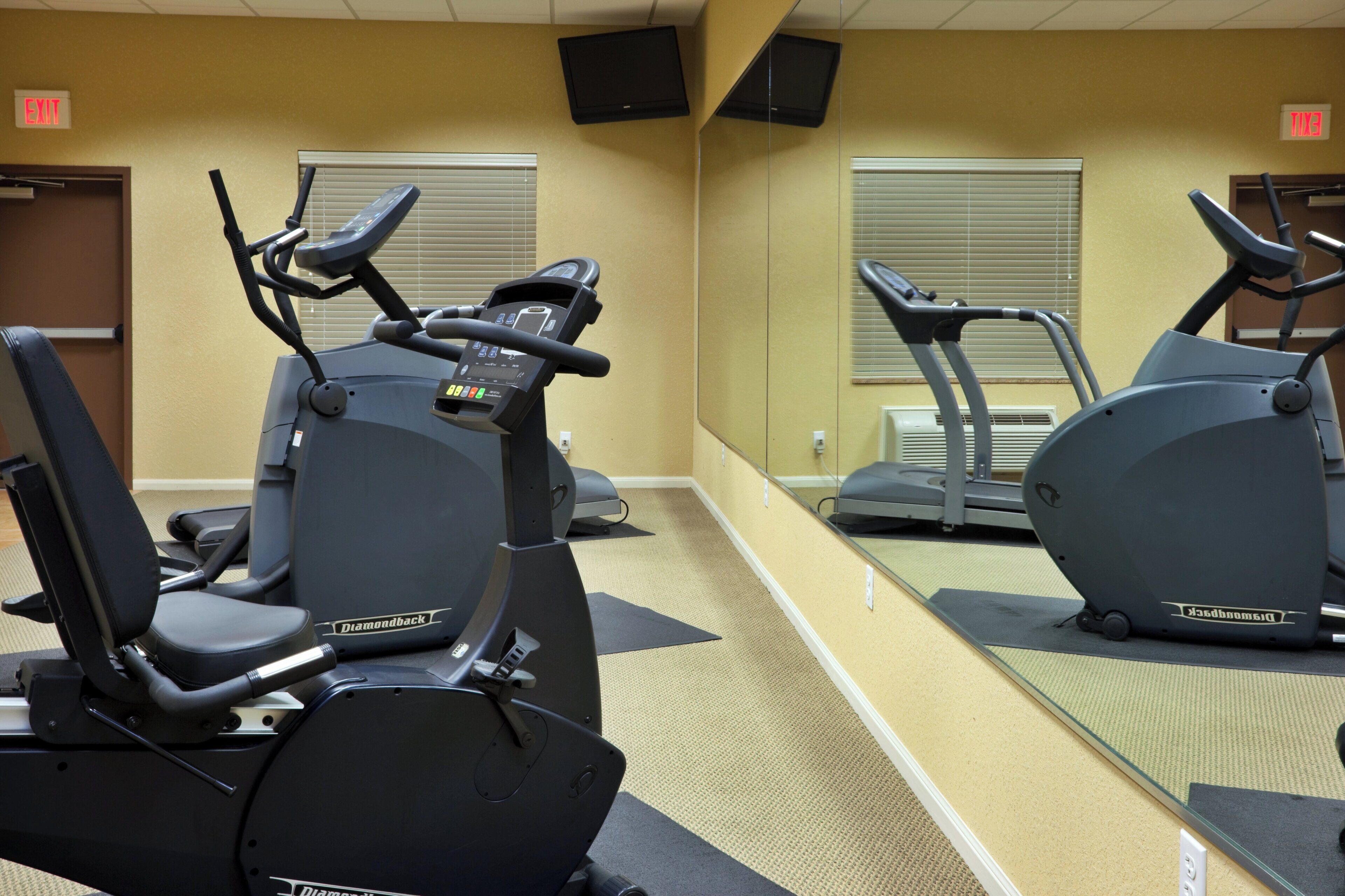 Un gimnasio con equipo de ejercicio, incluyendo cintas de correr y bicicletas estáticas, y un espejo grande.