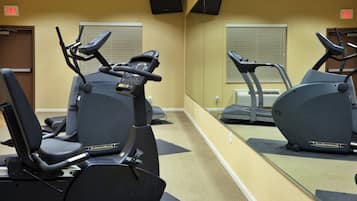 Un gimnasio con equipo de ejercicio, incluyendo cintas de correr y bicicletas estáticas, y un espejo grande.